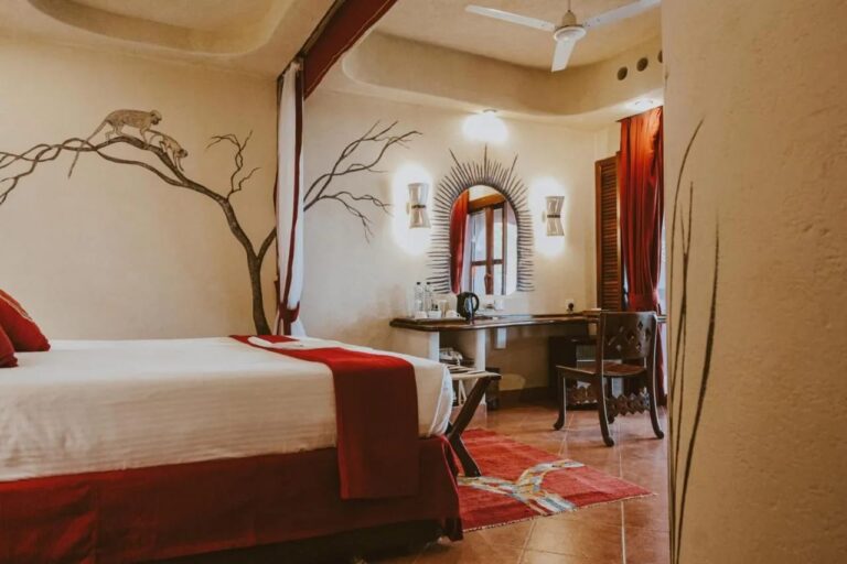 Una habitación con un árbol y dos monos pintados en la pared, y un escritorio bajo un espejo en forma de sol