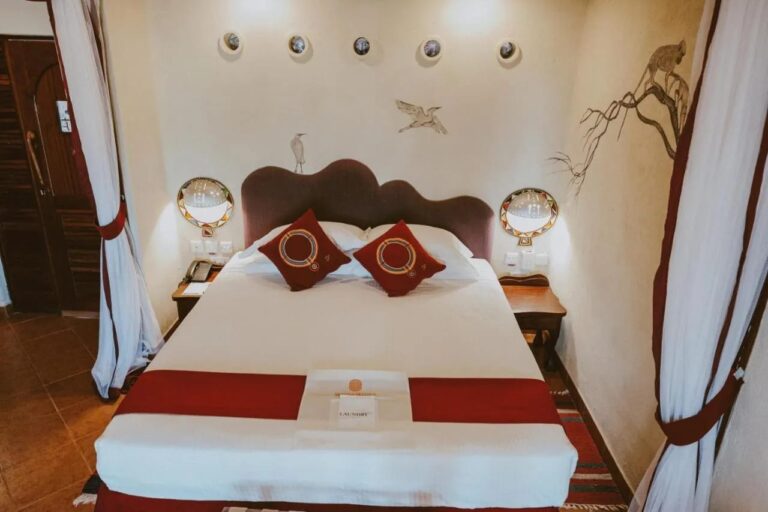 Una cama grande con cabecero ondulado, entre dos cortinas blancas atadas con un lazo rojo