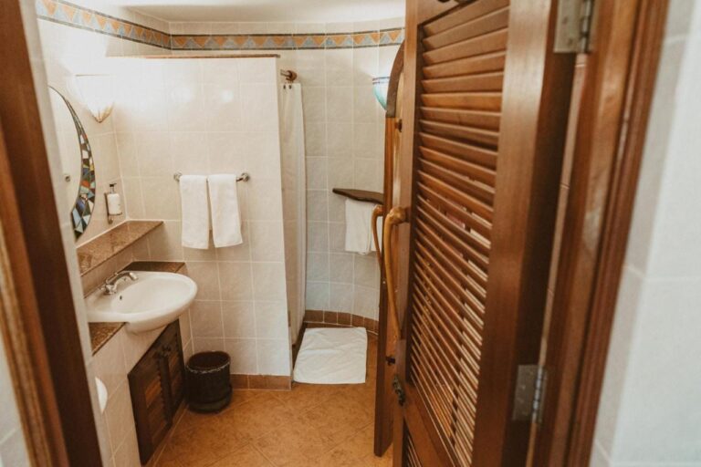 Un baño visto desde su puerta de madera con persianas, con un lavabo y una ducha con cortina