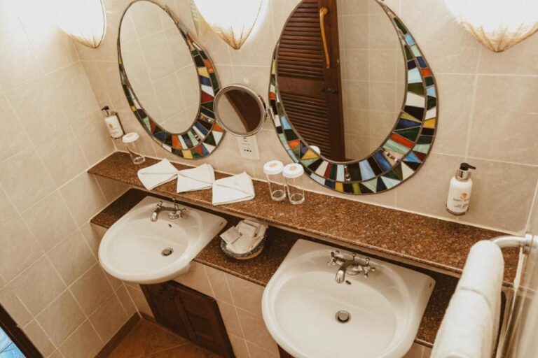 Un baño con dos lavabos y un espejo de aumento entre dos espejos de mosaico