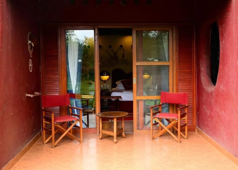 La terraza de una habitación entre dos muros rojos, con dos sillas plegables rojas y una mesa redonda