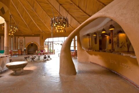 El mostrador de tierra esculpida de la recepción, grabado con el nombre del Amboseli Sopa Lodge, bajo un techo de juncos