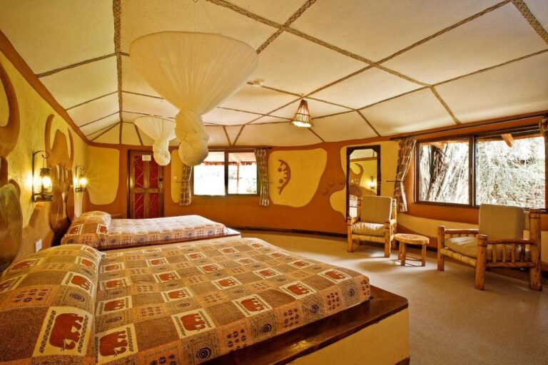 Una habitación con dos camas y colchas con motivos de elefantes, bajo mosquiteros anudados al techo