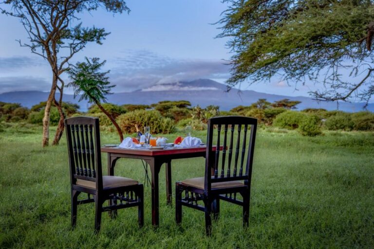 Una mesa puesta para dos sobre la hierba, bajo las acacias, con el Kilimanjaro a lo lejos