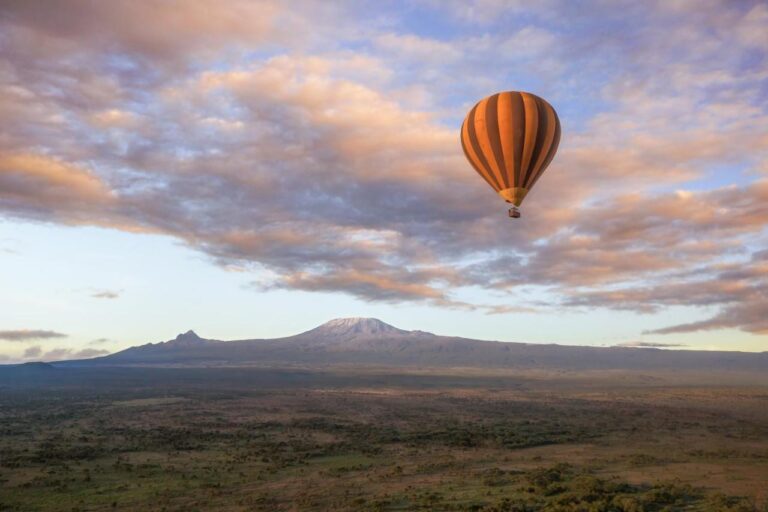 Un globo aerostático sobre la llanura, con el Kilimanjaro en el horizonte bajo un cielo rosa