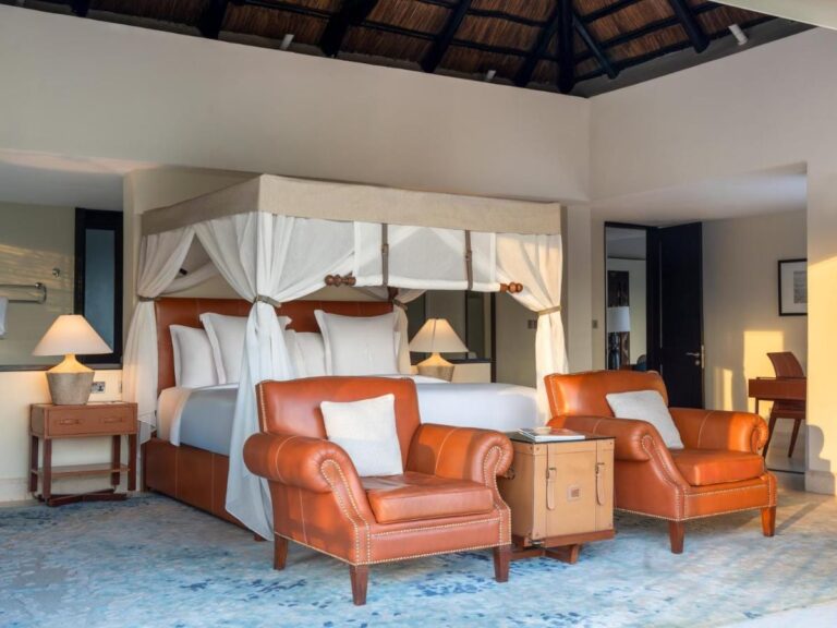 Una habitación con cama con dosel y dos sillones de cuero naranja