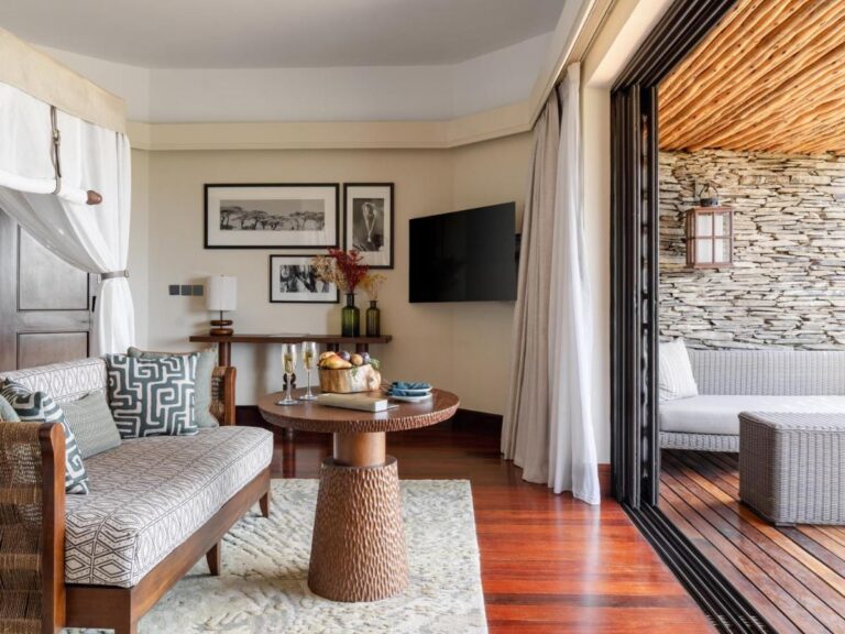 La zona de estar de una habitación, con un banco tapizado, dos copas sobre una mesita y la terraza tras el ventanal abierto