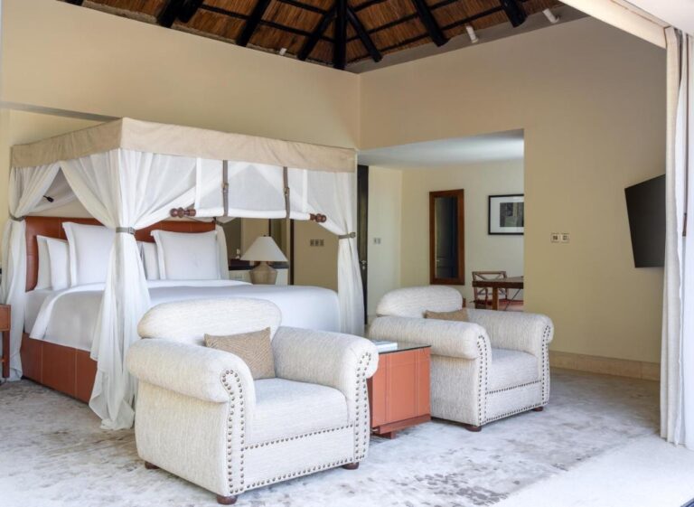 Una habitación con cama con dosel y dos sillones blancos capitonados