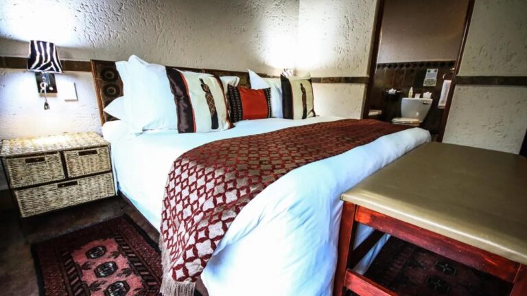 Una cama grande con una colcha roja y blanca, junto a una mesita de noche con cestas de mimbre