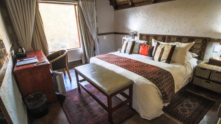 Una habitación con una cama grande, un escritorio bajo la ventana y un banco acolchado