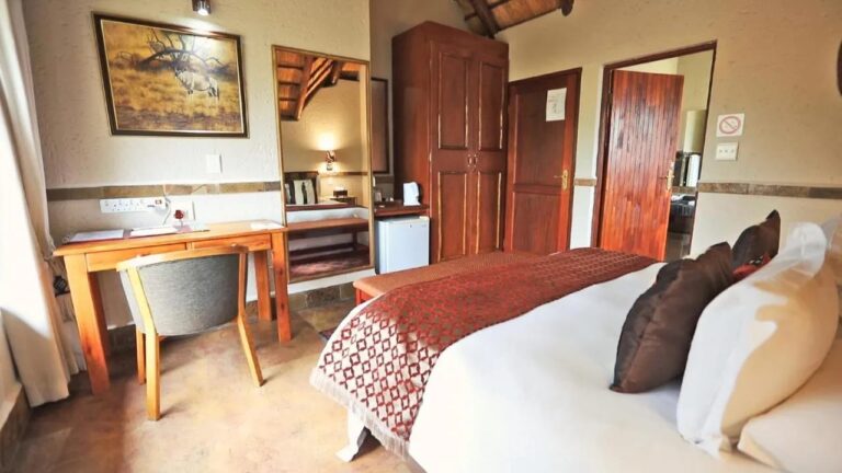 Una habitación con un escritorio, un armario de madera, un pequeño refrigerador y el cuadro de un órix en la pared