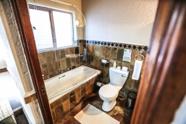 Un baño con bañera e inodoro, con las paredes revestidas de piedra