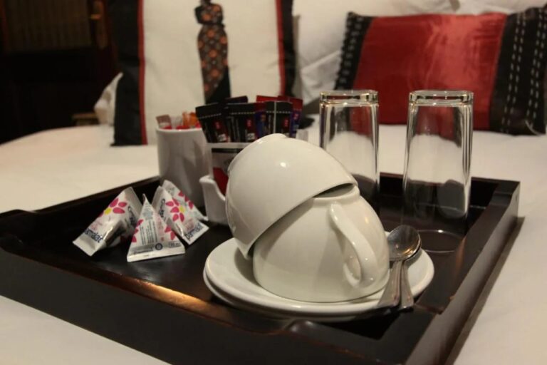 Una bandeja con tazas, vasos y sobres de té y café, sobre una cama