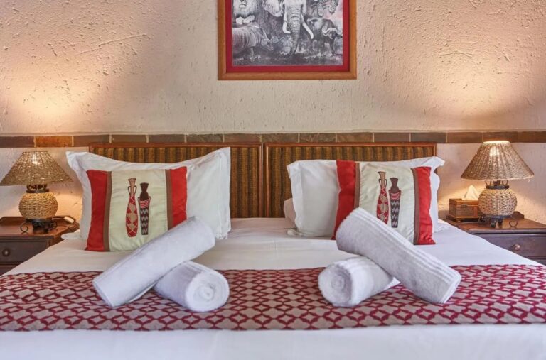 Una cama grande con toallas enrolladas, bajo una imagen en blanco y negro de un león, un elefante, un rinoceronte y un búfalo