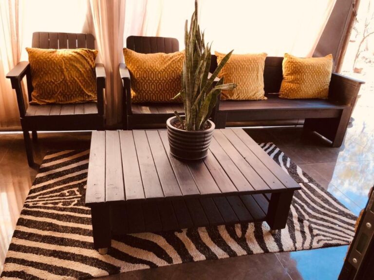 Un salón con asientos de madera oscura, cojines amarillo mostaza y una mesa baja sobre una alfombra con estampado de cebra