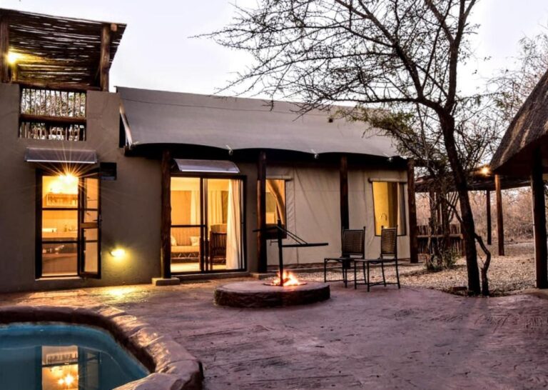 Una tienda del Jackalberry Ridge iluminada al anochecer, con su piscina privada, el fuego encendido y dos sillas en la terraza