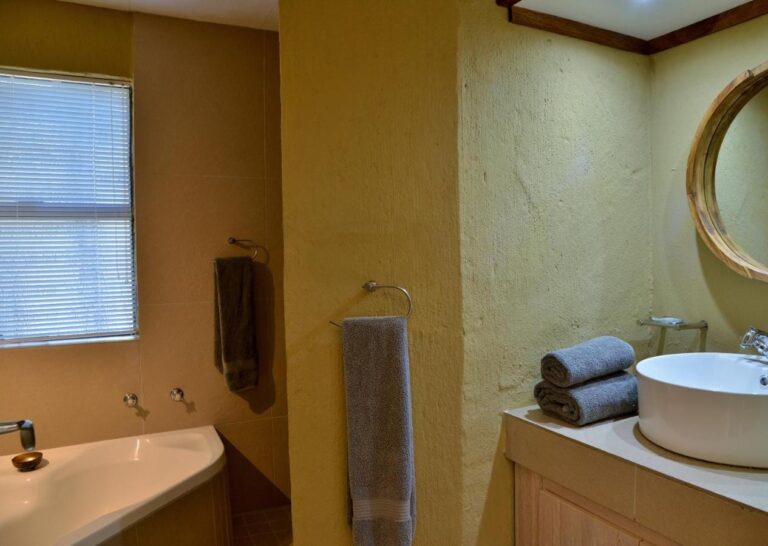 Un baño con bañera, un lavabo redondo sobre la encimera y un espejo redondo con marco de madera