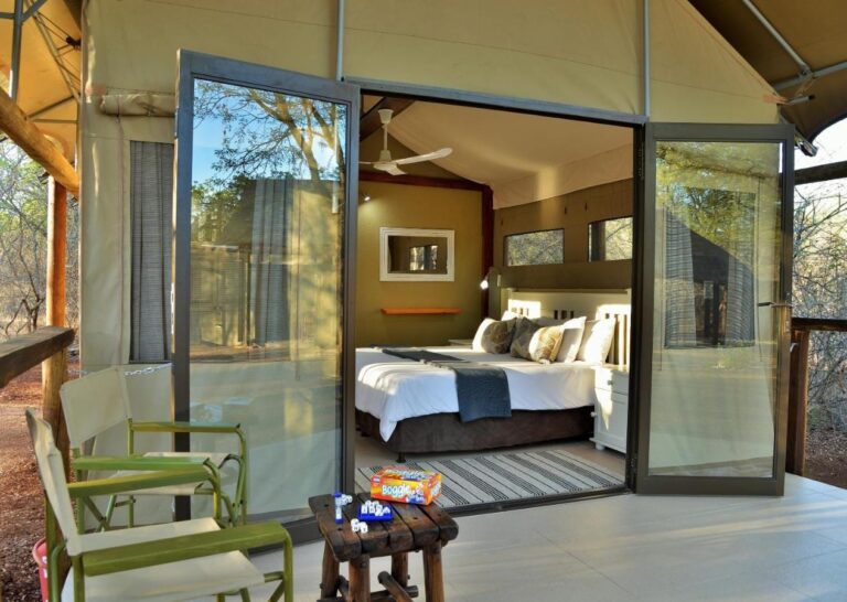 Una tienda vista desde su terraza, con las puertas de cristal abiertas hacia la cama y sillones verdes delante