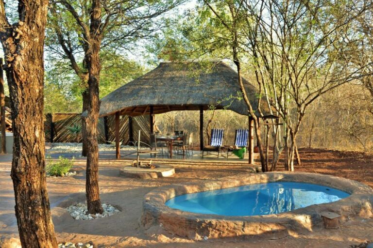 Una piscina redonda delante de una zona cubierta con techo de paja, con una mesa de comedor y dos tumbonas de rayas