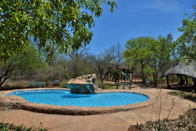 La piscina con cascada del Jackalberry Ridge bajo un cielo azul, rodeada de bancos y árboles