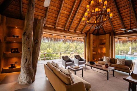 El salón del Kapama River Lodge bajo un alto techo de paja, abierto a una piscina y a la sabana