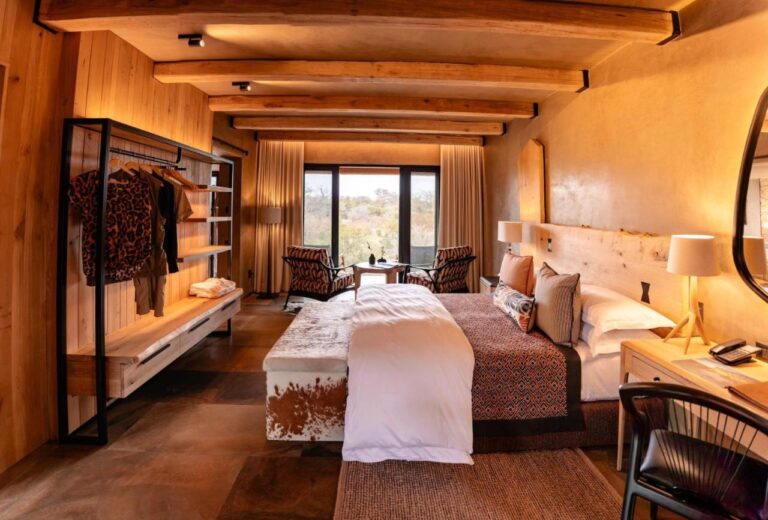 Una suite con una cama grande, un banco de piel de vaca y un armario abierto