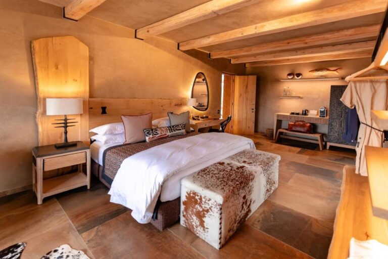Una suite con cama grande, un banco de piel de vaca, un rincón de café y un albornoz colgado
