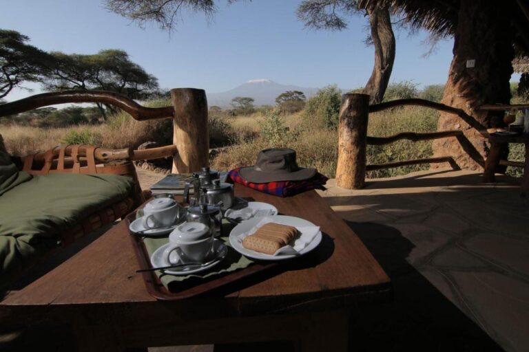 Una bandeja de té y galletas en una terraza, con un sombrero de safari, y el Kilimanjaro detrás de las acacias
