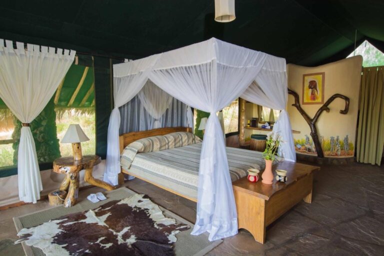 Una tienda de paredes verde oscuro, con una cama bajo un mosquitero, un baúl y una piel de vaca en el suelo