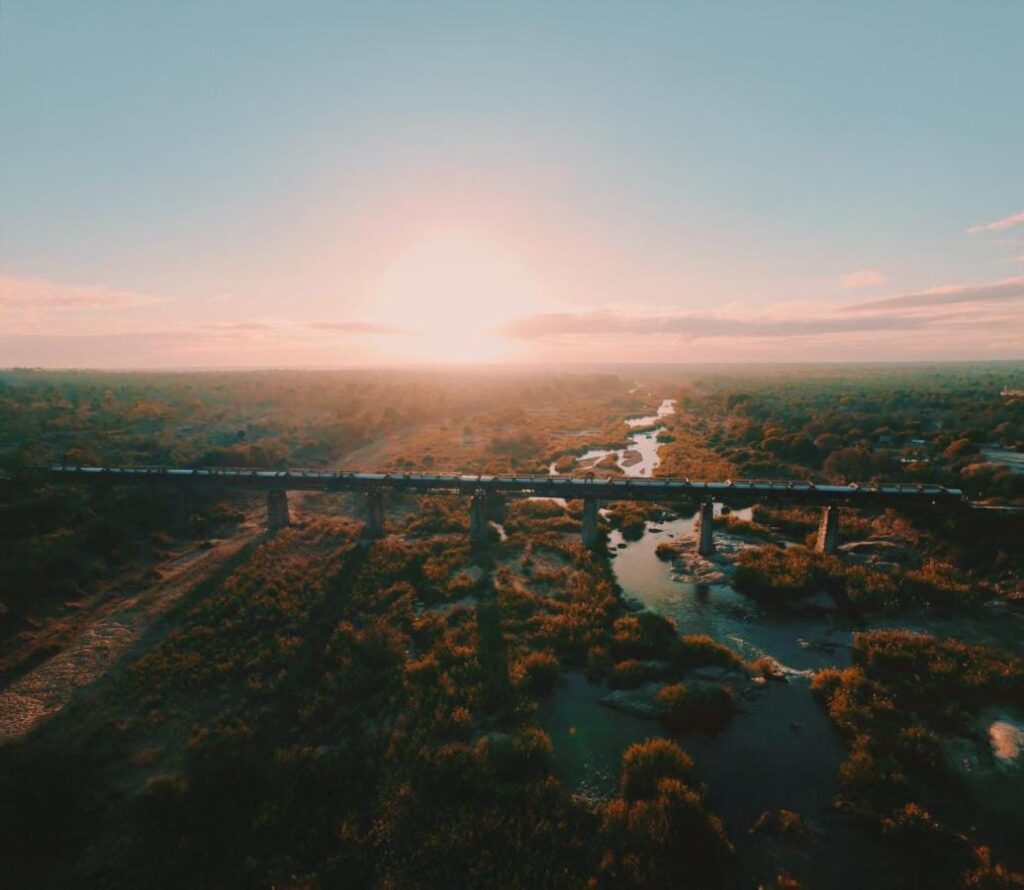 El tren del Kruger Shalati sobre el puente del Selati, visto desde el aire, encima del río y la sabana, con el sol bajo en el horizonte