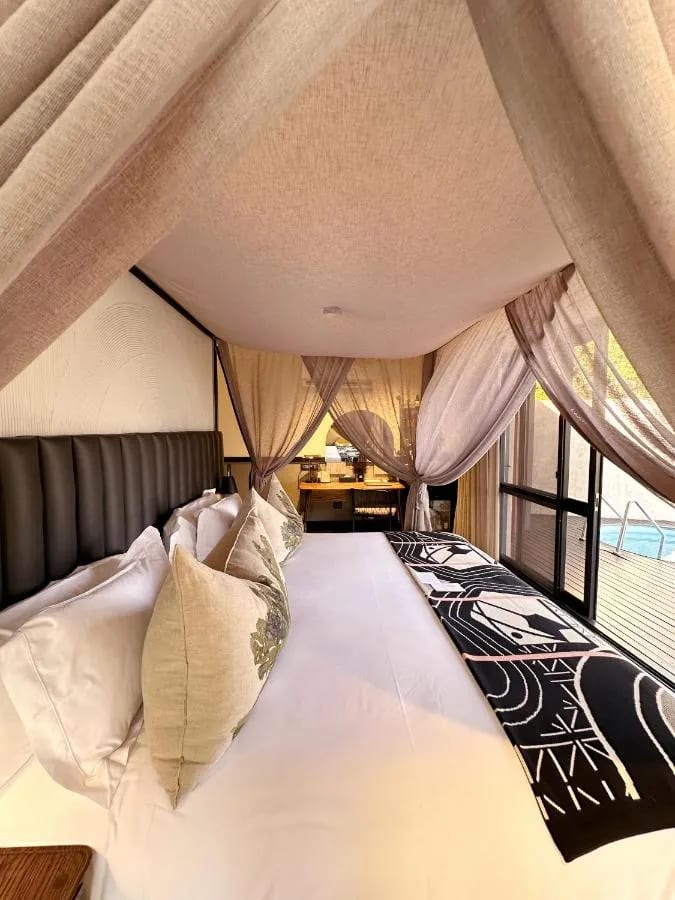 La cama grande de una suite bajo sus visillos, con la pequeña piscina detrás del ventanal