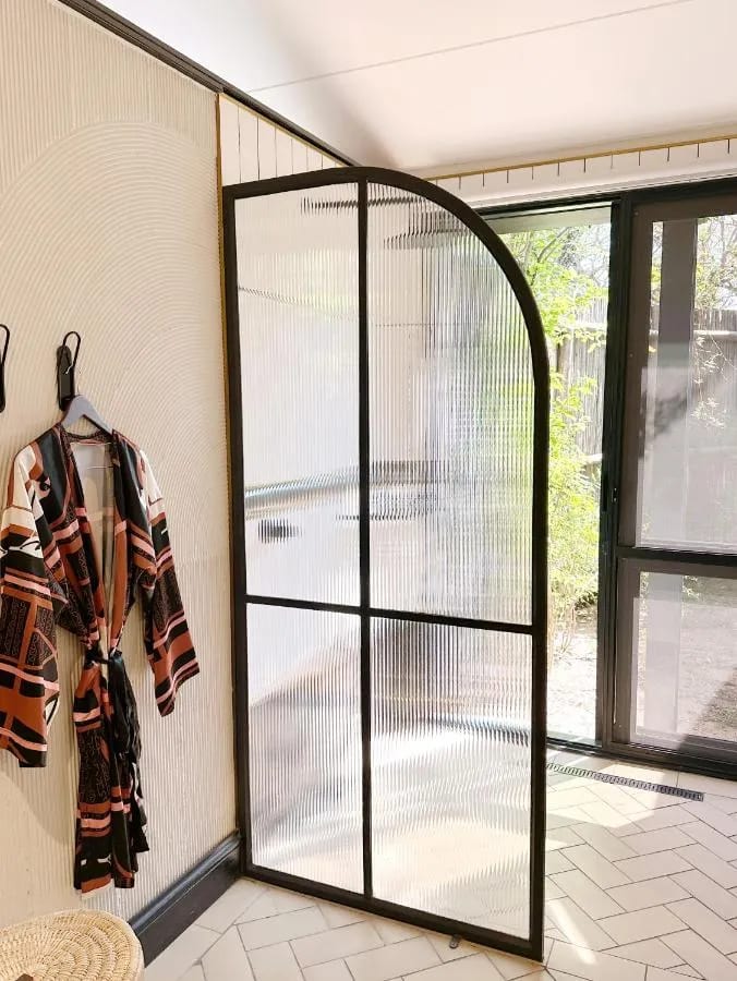 Una ducha detrás de una puerta de vidrio en arco, con un albornoz estampado colgado en la pared