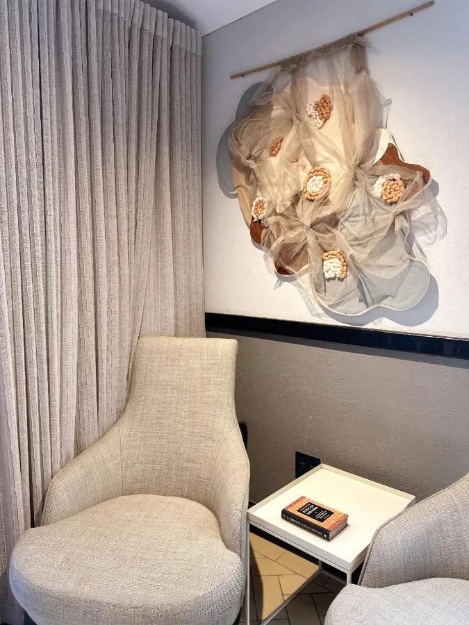 Dos sillones claros alrededor de una mesita, bajo una decoración de tela en la pared