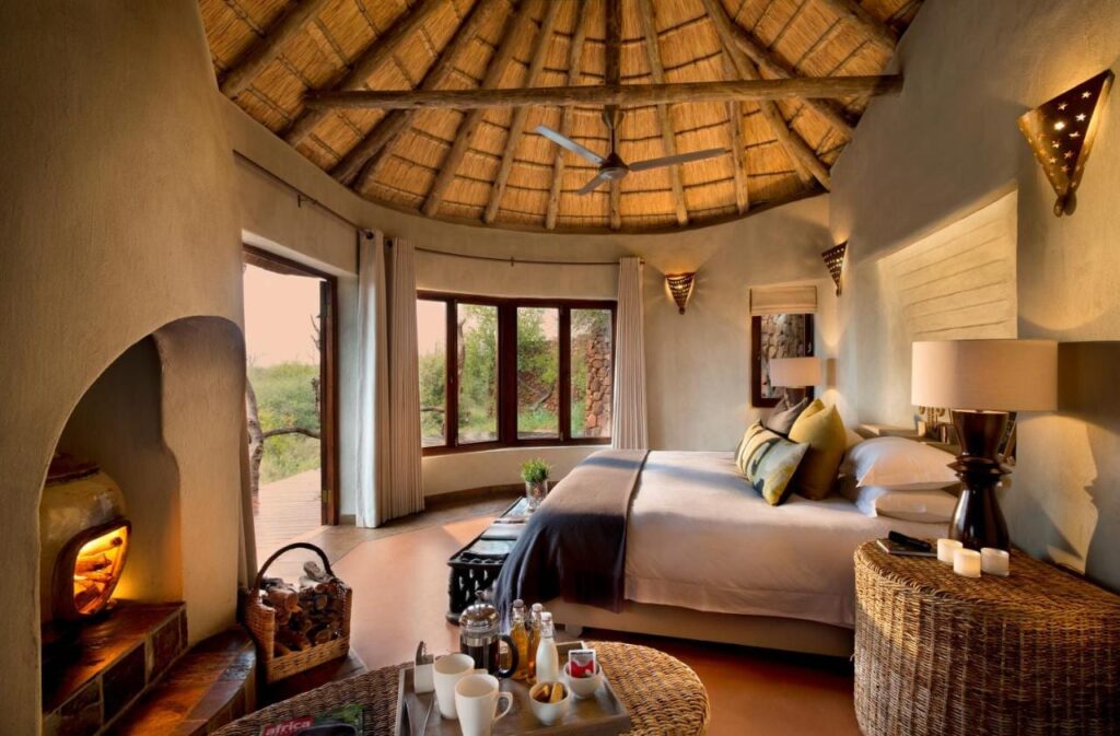 Una suite del Madikwe Safari Lodge bajo un techo de paja, con una cama grande y una chimenea encendida