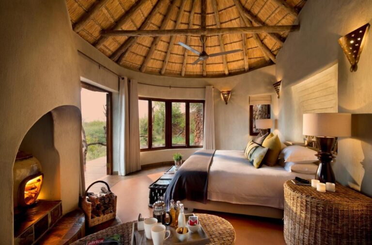 Una suite del Madikwe Safari Lodge bajo un techo de paja, con una cama grande y una chimenea encendida