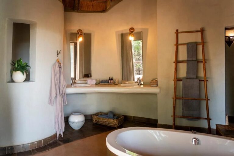Un baño de paredes curvas, con una bañera, dos lavabos y un toallero de escalera