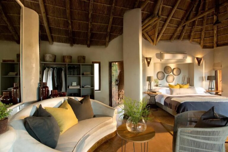 Una suite del Madikwe Safari Lodge con un sofá blanco curvo, una cama grande y un armario abierto