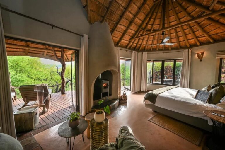 Una suite abierta a una terraza frente a los árboles, con una estufa de leña y una cama grande