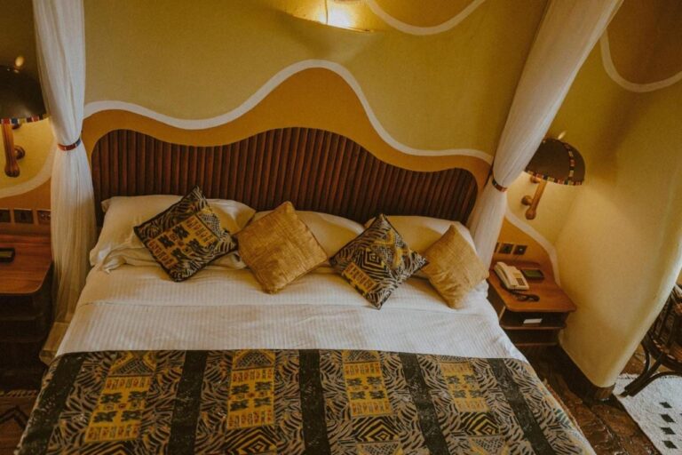 Una cama grande con cojines de motivos africanos, bajo un cabecero de listones de madera y paredes pintadas con ondas