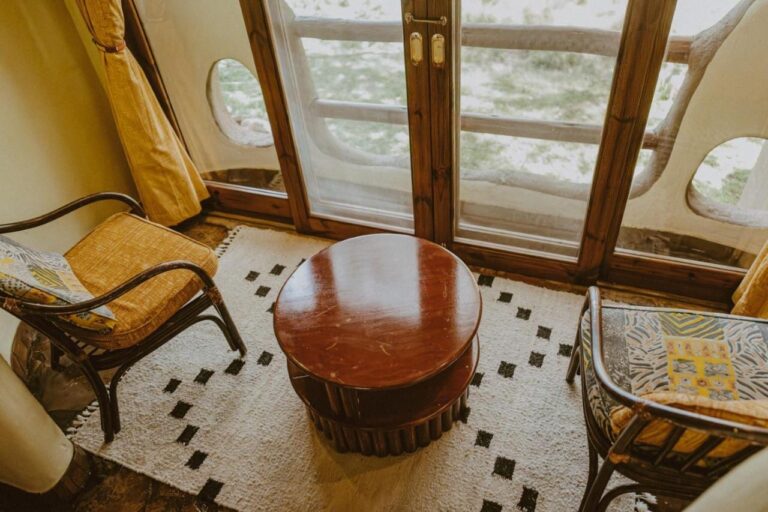 Dos sillones y una mesa redonda delante de una puerta acristalada, con la sabana tras la barandilla del balcón