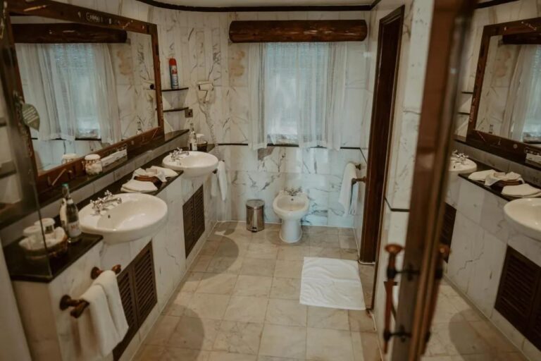 Un baño de mármol blanco, con dos lavabos, un secador de pelo de pared y un bidé bajo la ventana