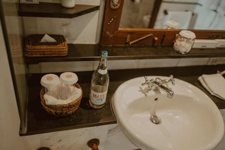 Un lavabo con una botella de agua, algodones y una caja de pañuelos de mimbre
