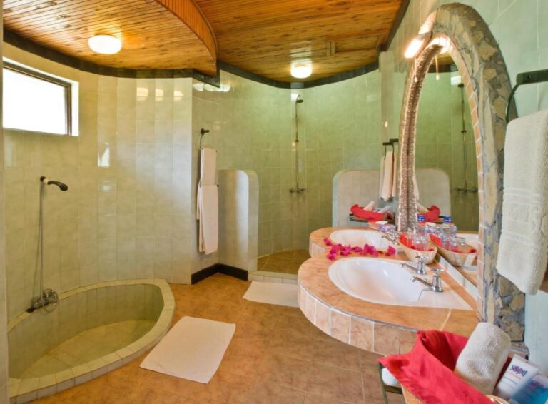 Un baño de azulejos verdes, con un plato de ducha redondo empotrado y dos lavabos bajo un espejo en arco
