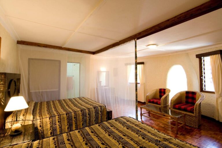 Una habitación con dos camas bajo mosquitero, con dos sillones de cojines a cuadros rojos