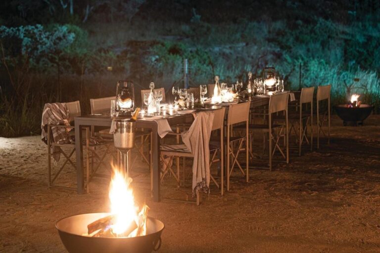 Una larga mesa puesta para la cena al aire libre, entre faroles y fuegos en braseros