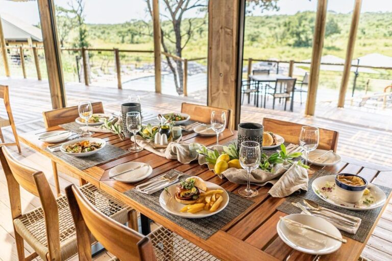 Una mesa servida en el restaurante, abierta a la terraza, la piscina y la sabana
