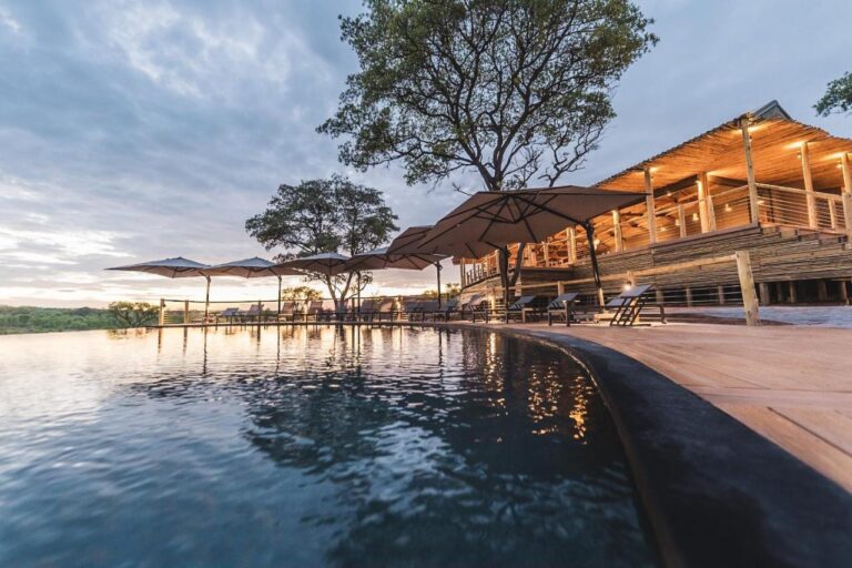 La piscina infinita del Mdluli Safari Lodge y su edificio principal iluminado, bajo un cielo nublado