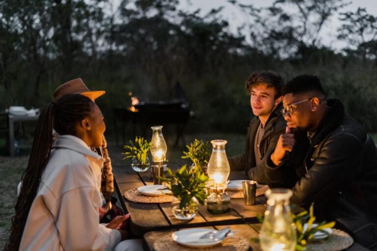 Comensales en una mesa al aire libre, iluminada con lámparas de aceite, al caer la noche