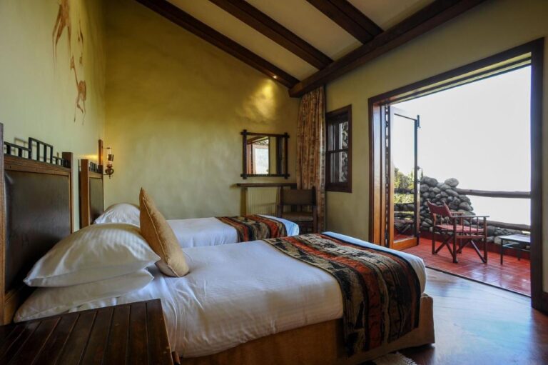 Una habitación con dos camas abierta a un balcón, con un sillón de lona roja
