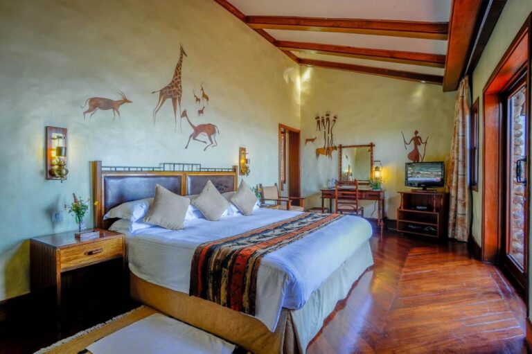 Una habitación con una cama grande, un escritorio, una televisión y una jirafa pintada en la pared